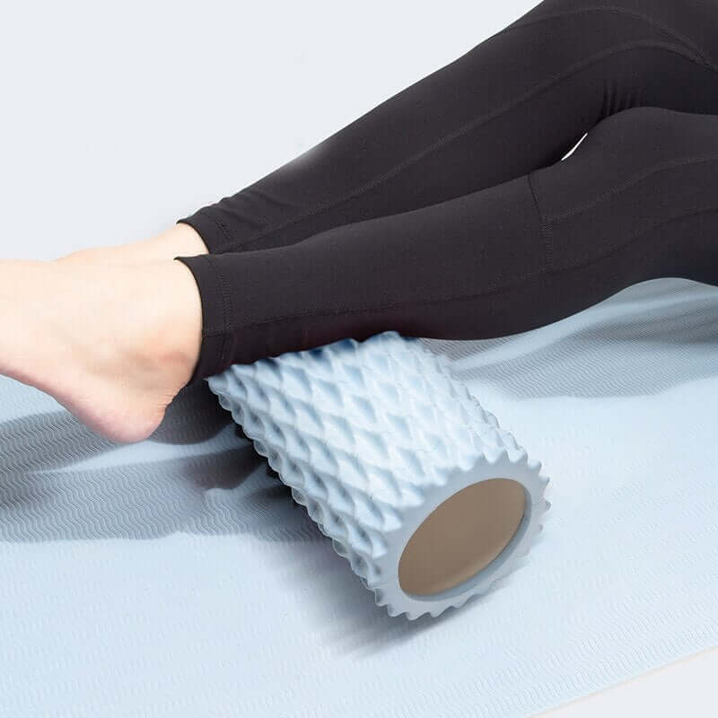 Person using an ocean blue foam massage roller on yoga mat for muscle relief and relaxation.